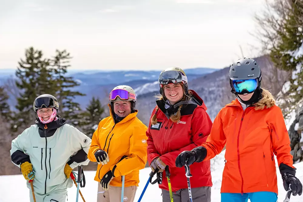 Four female skiers pose together at Killington Mountain with scenic views in the background.