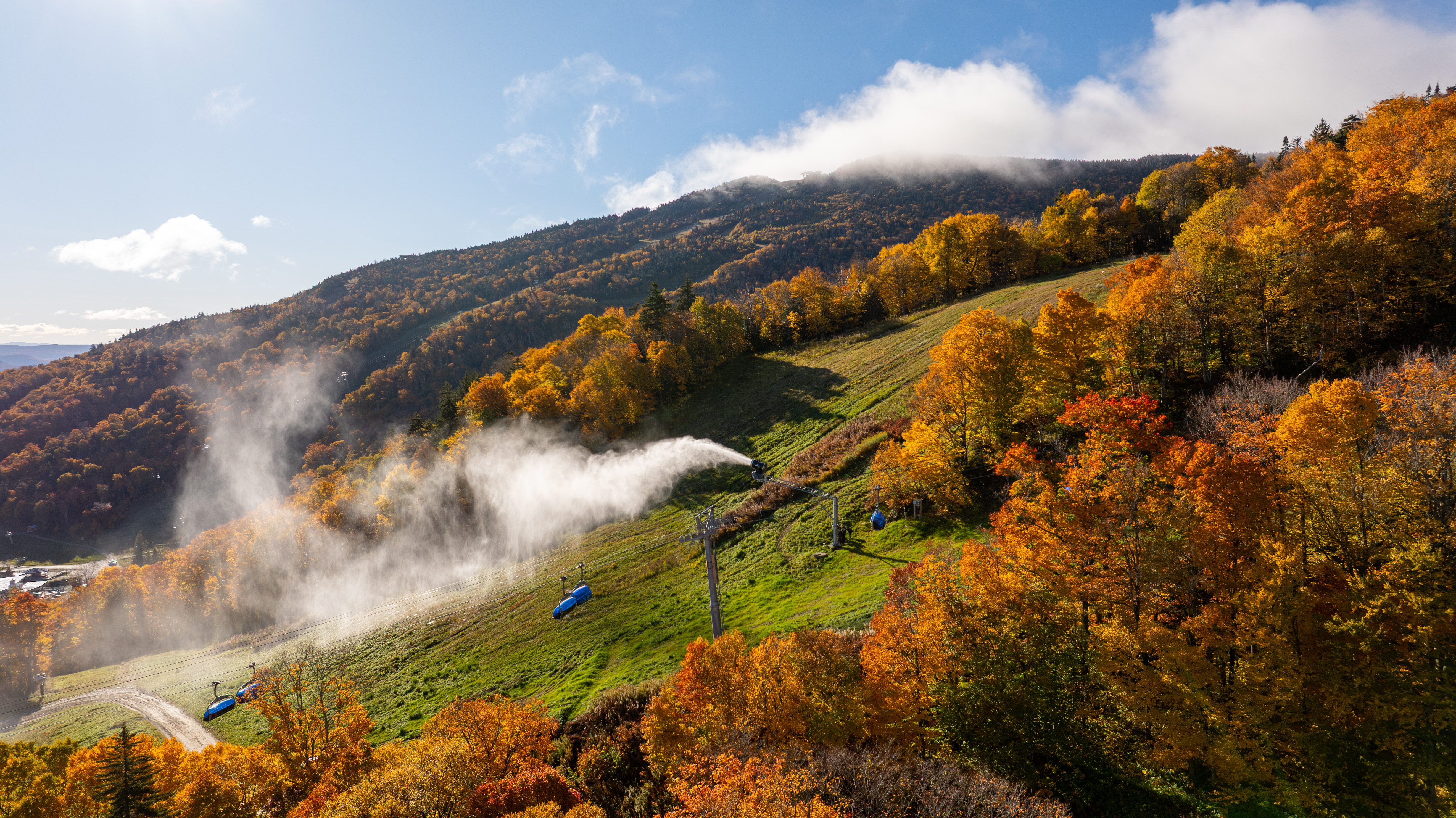 Autumn landscape with colorful trees and snowmaking equipment on a mountainside.