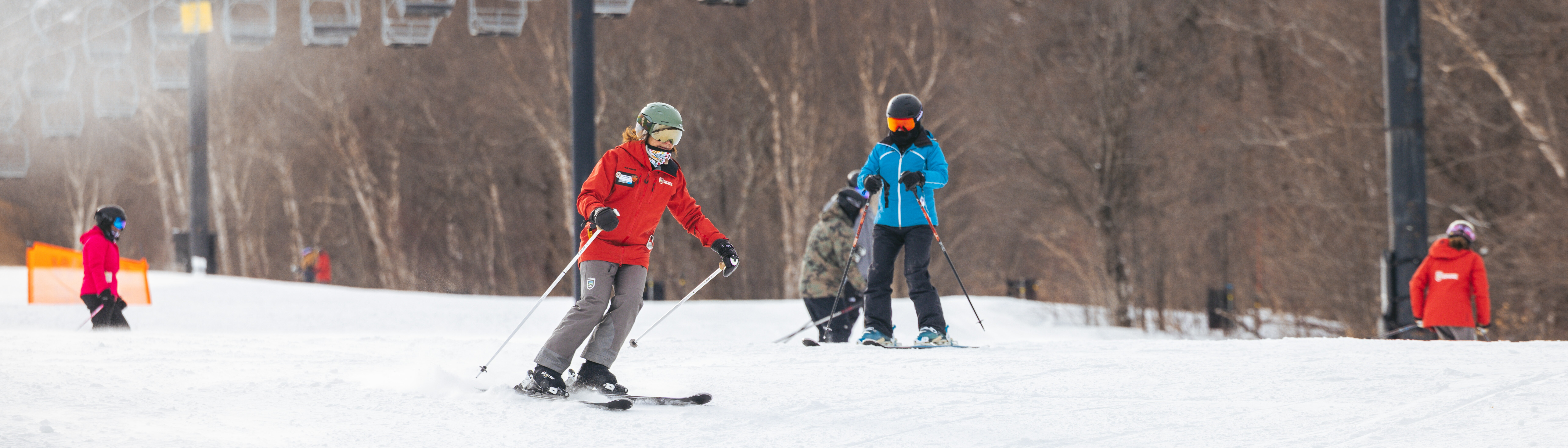Skiers on snowy slopes with a ski lift in the background.