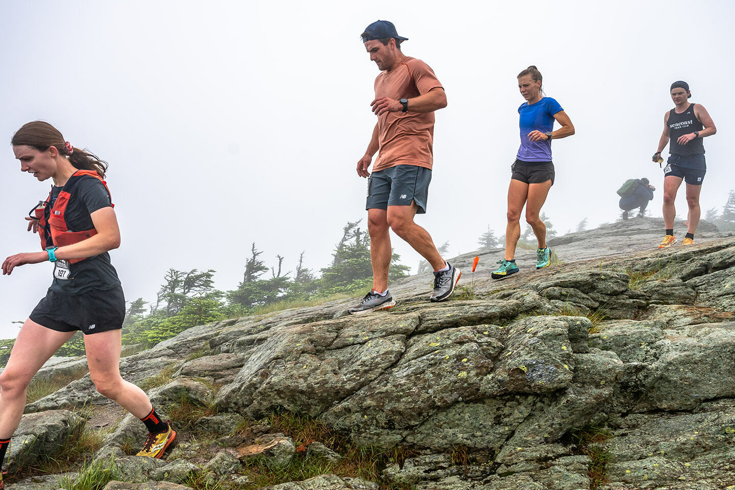 Runners navigate rocky terrain in foggy conditions during a trail race.