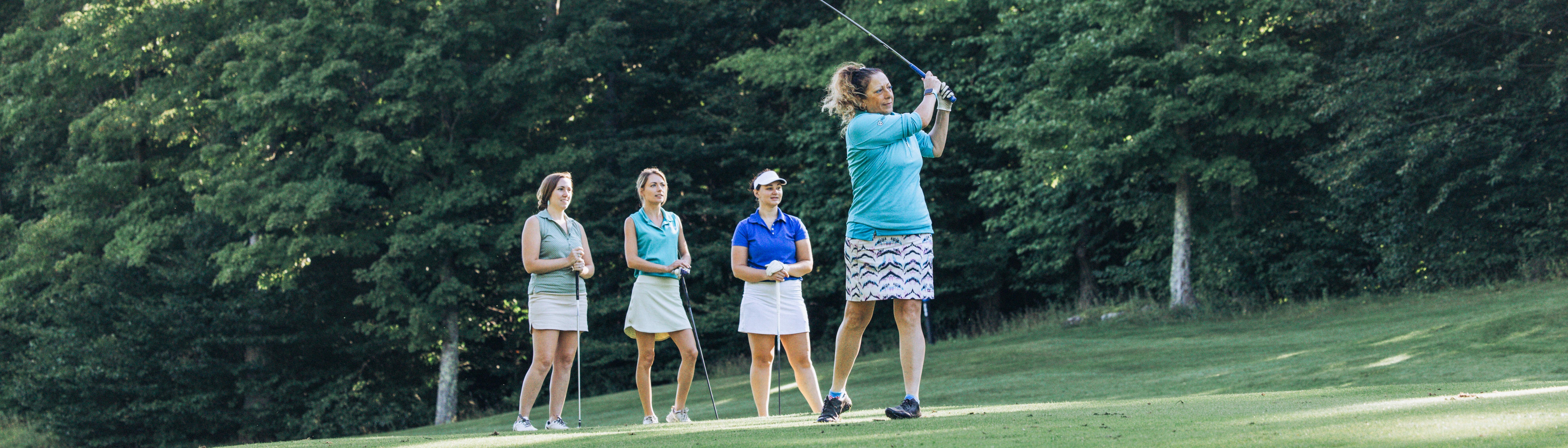 A woman swings a golf club while three others watch attentively on the course.