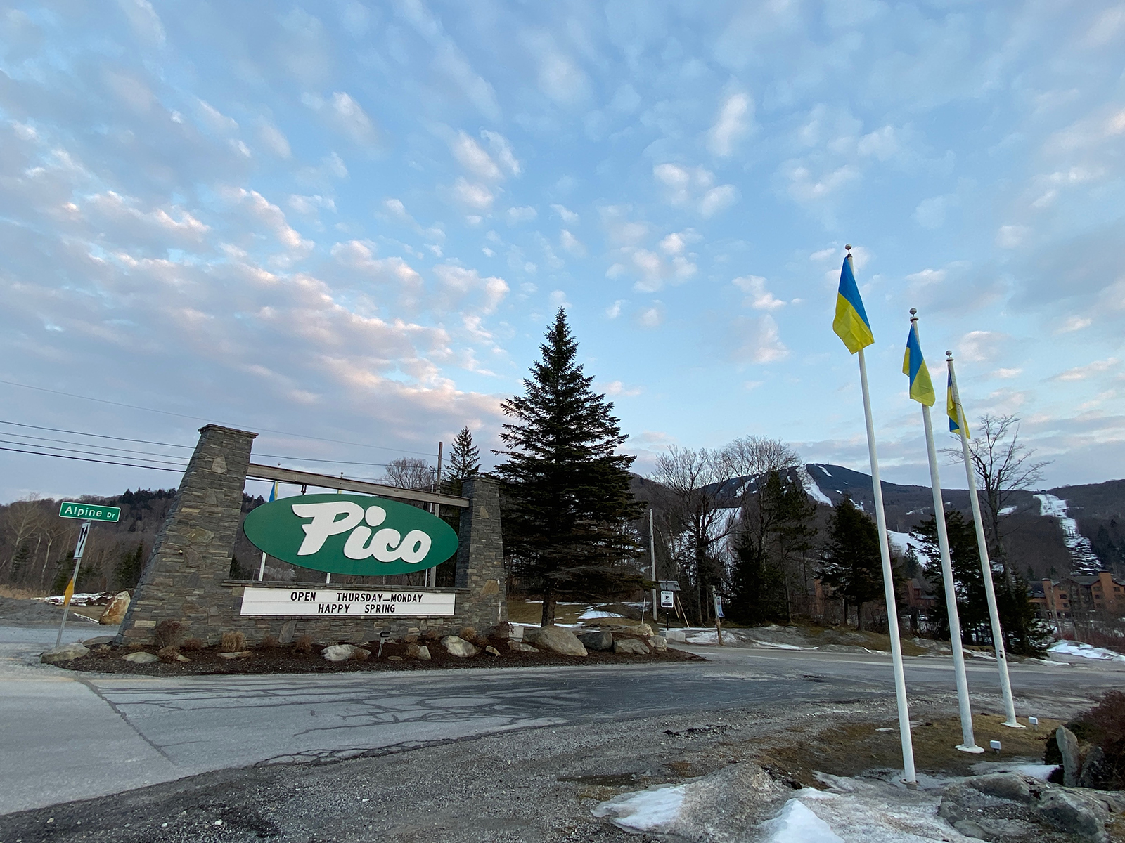 Pico Mountain welcome sign with flags, mountain in background, under a cloudy sky.