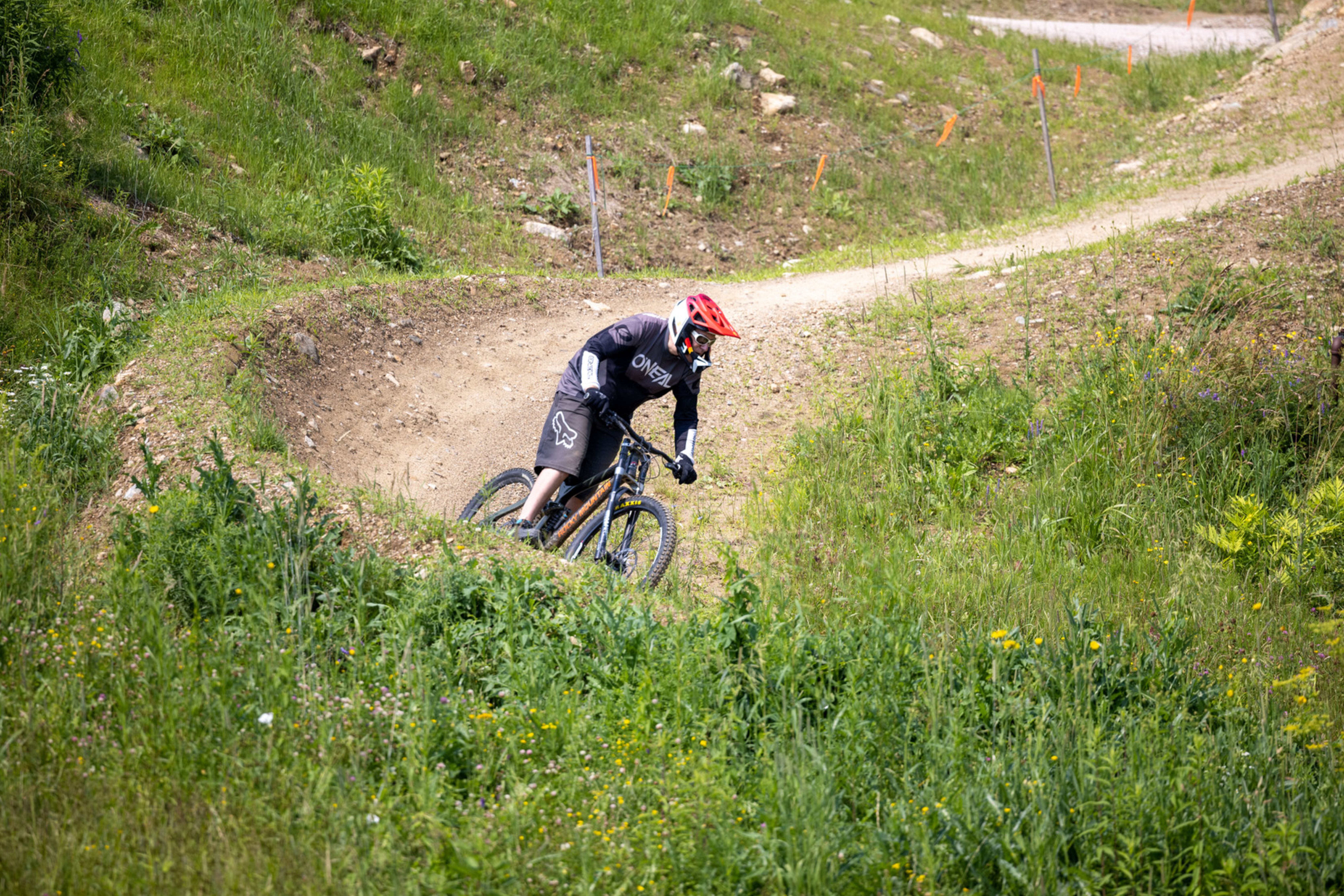A mountain biker navigating a dirt curve surrounded by greenery.