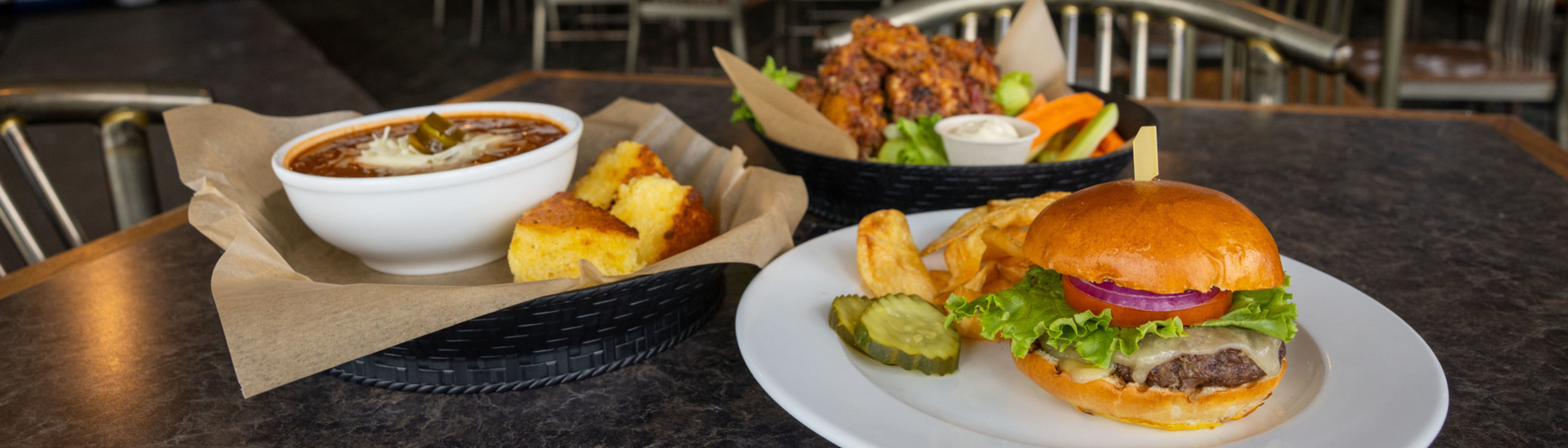 A plate with a burger, fries, pickles, and a bowl of chili with cornbread.
