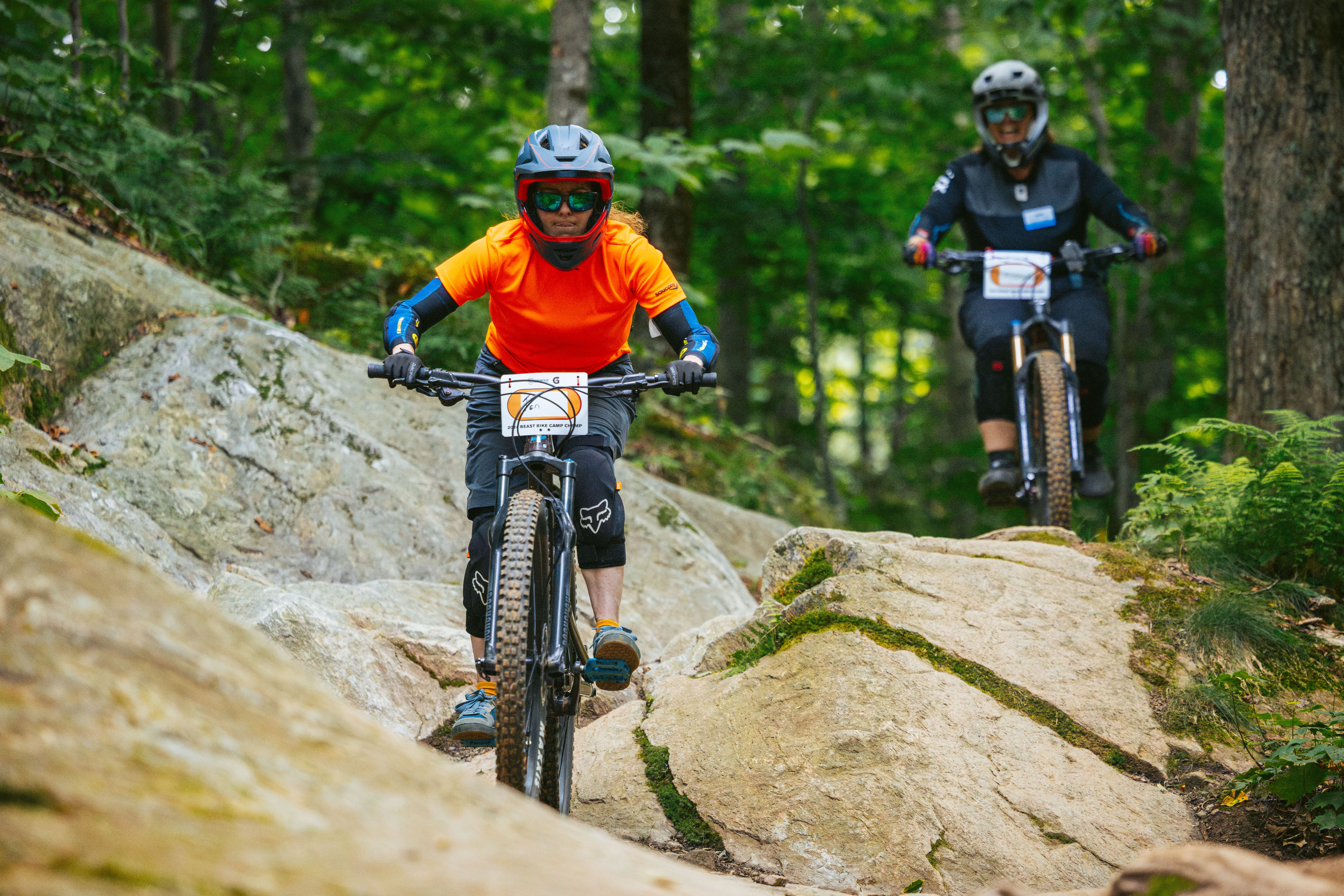 Two mountain bikers navigate rocky terrain in a lush forest.