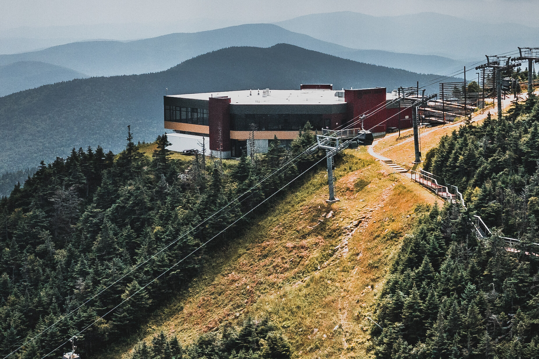 A modern building atop a hill with ski lifts and mountainous landscape in the background.