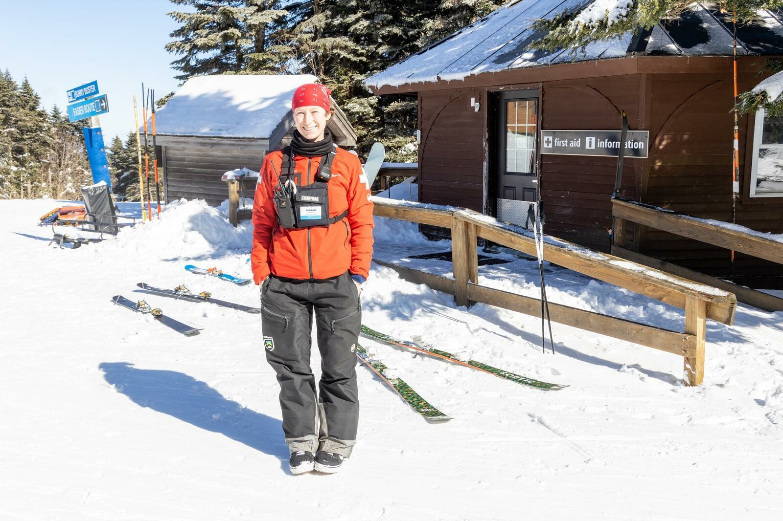 A patroller stands on snow near a first aid station and skis.