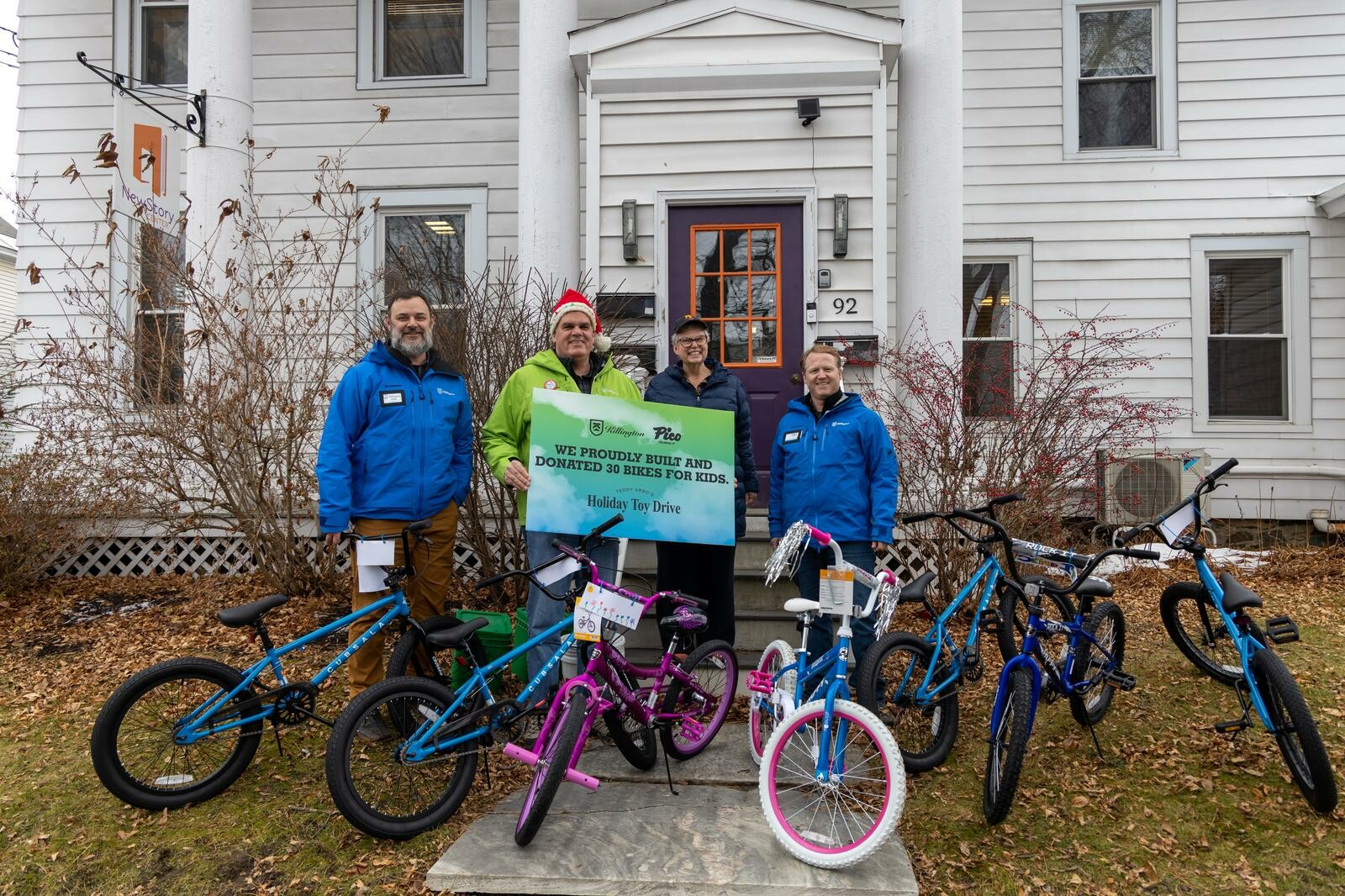 Four people stand with donated bikes outside a building for a holiday toy drive.