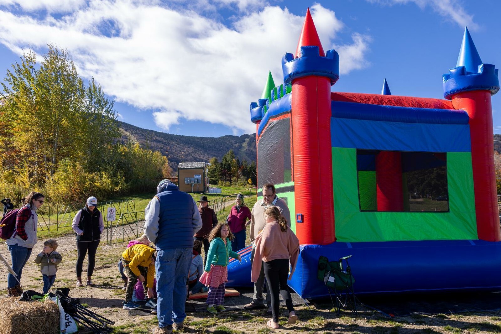 A colorful bounce house with children and adults gathered around in a park setting.