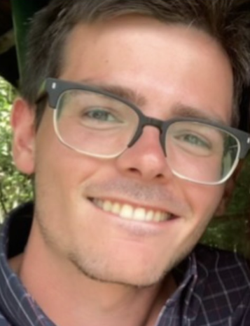 A smiling young man with glasses, posing outdoors in a casual shirt.