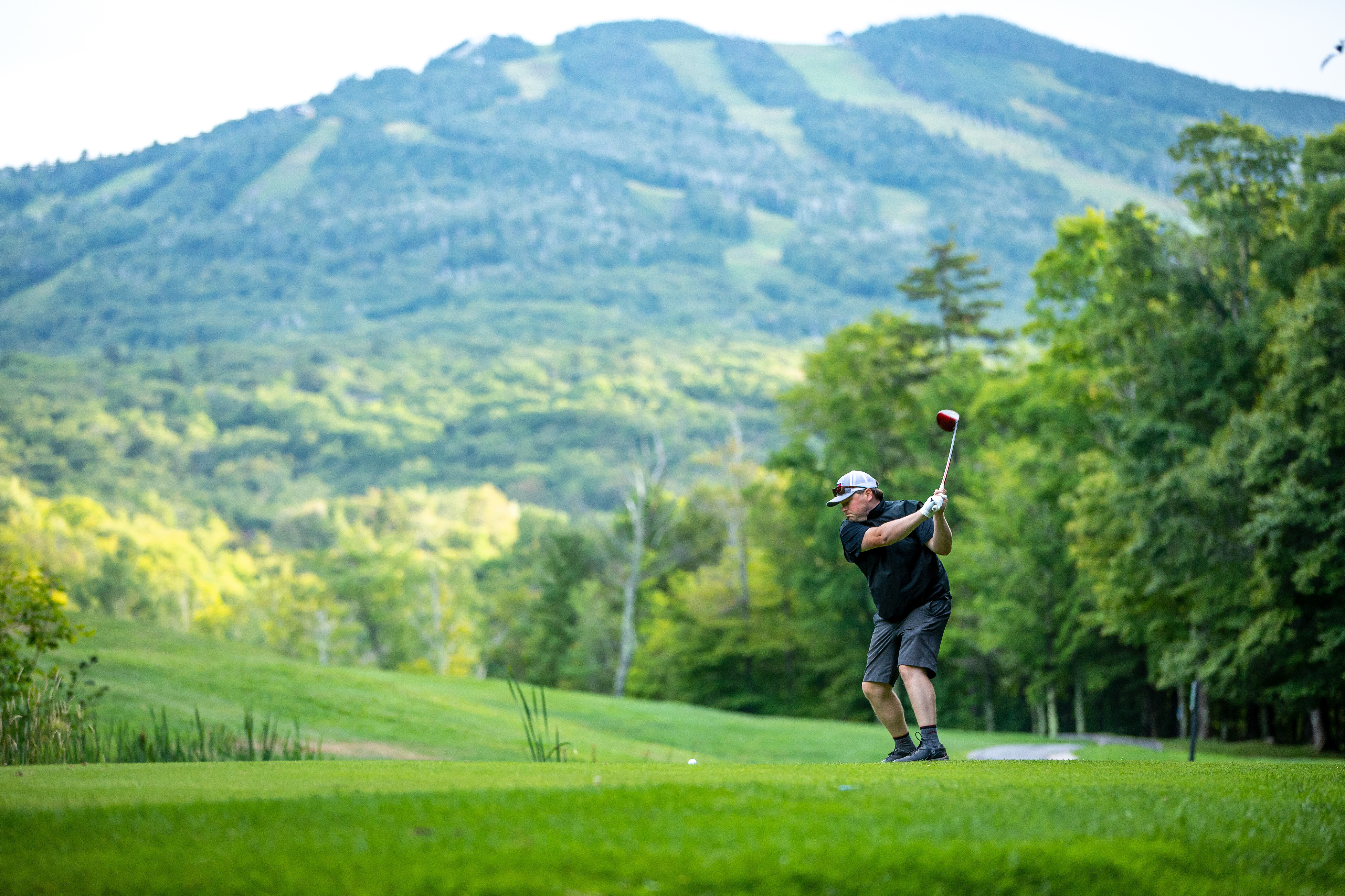Golfer swinging a club with a mountain landscape in the background.