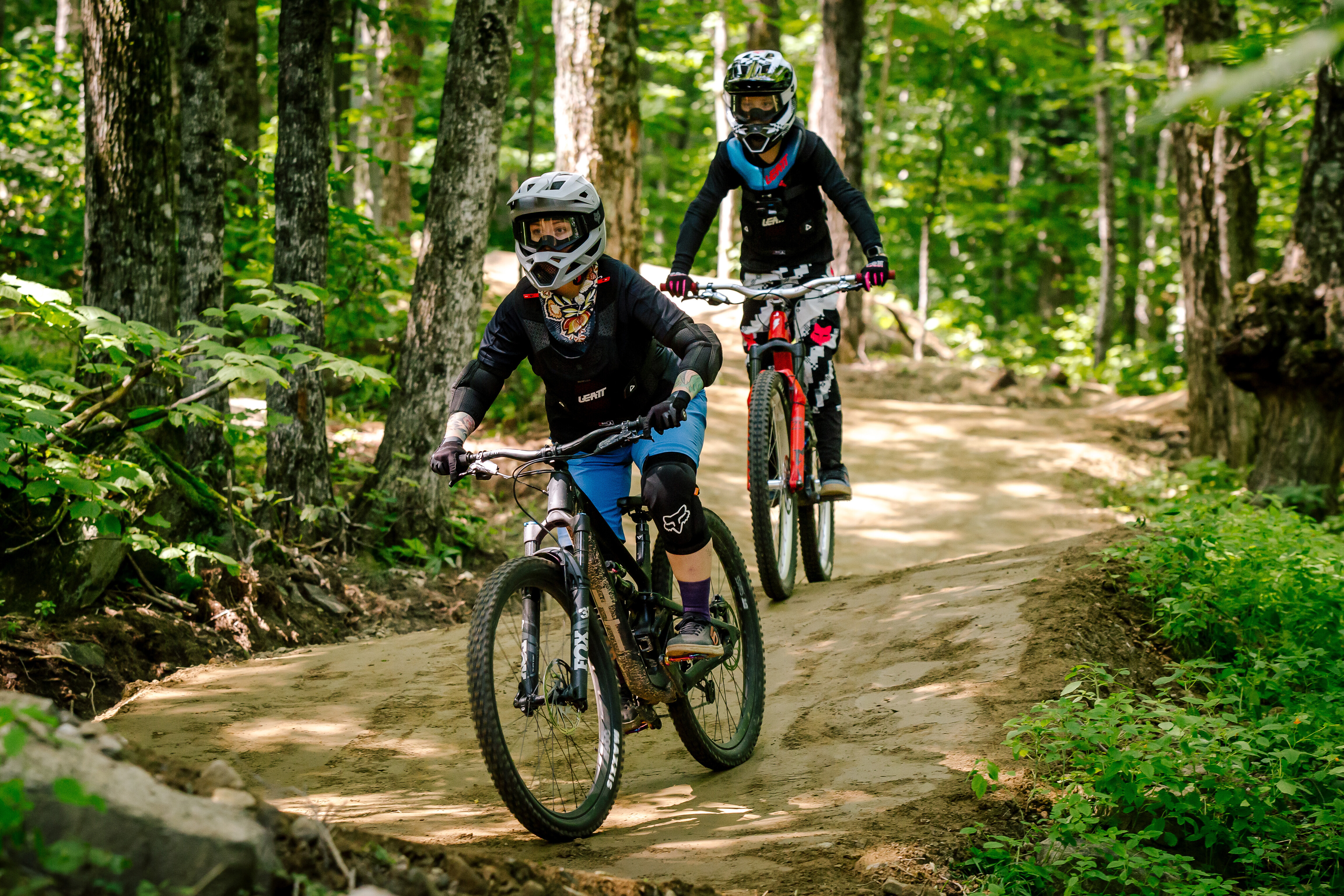 Two mountain bikers riding on a dirt path through a lush green forest.