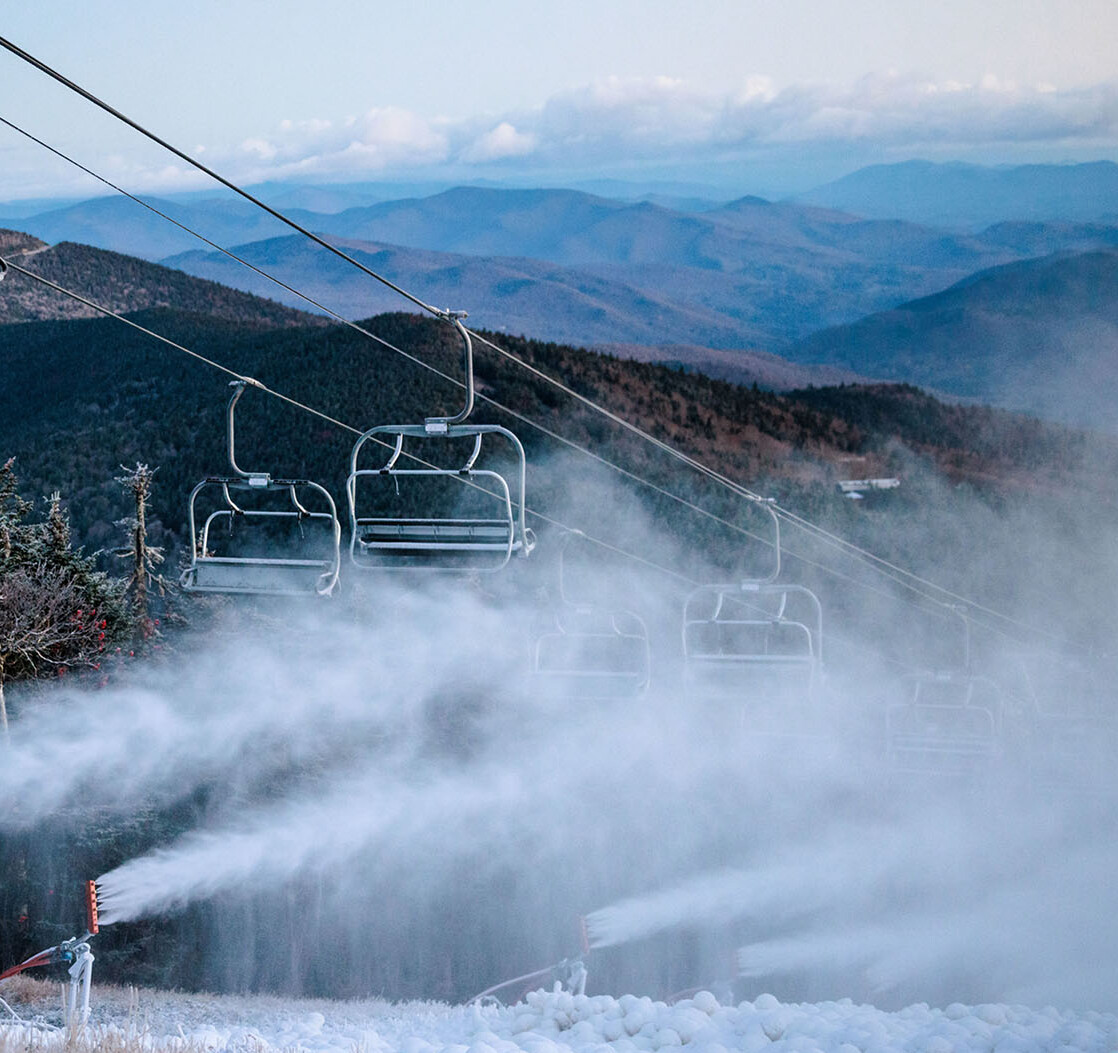 Ski lift with snowmaking machines in a misty mountain landscape.