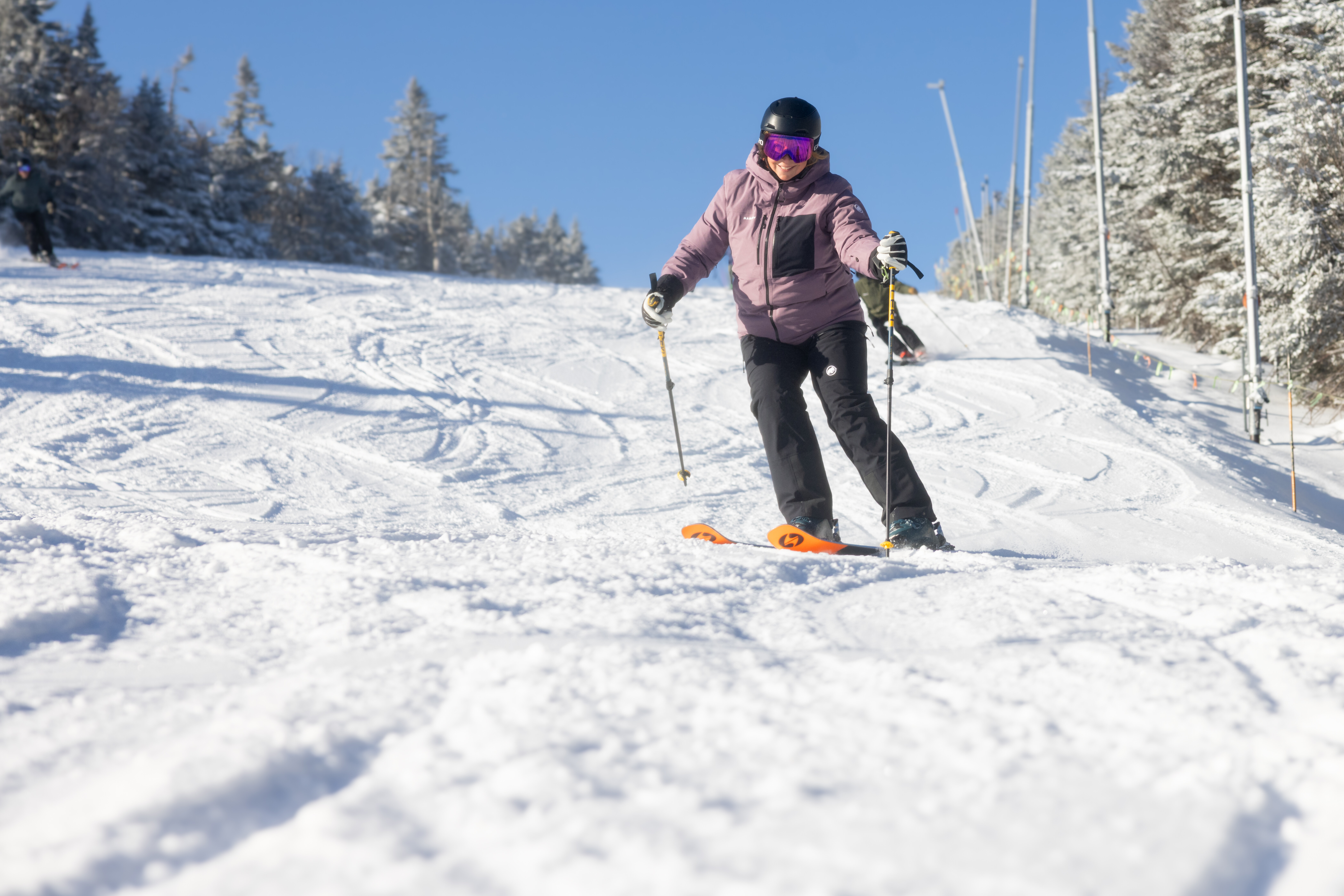 A skier in a pink jacket navigates down a snowy slope under a clear blue sky.