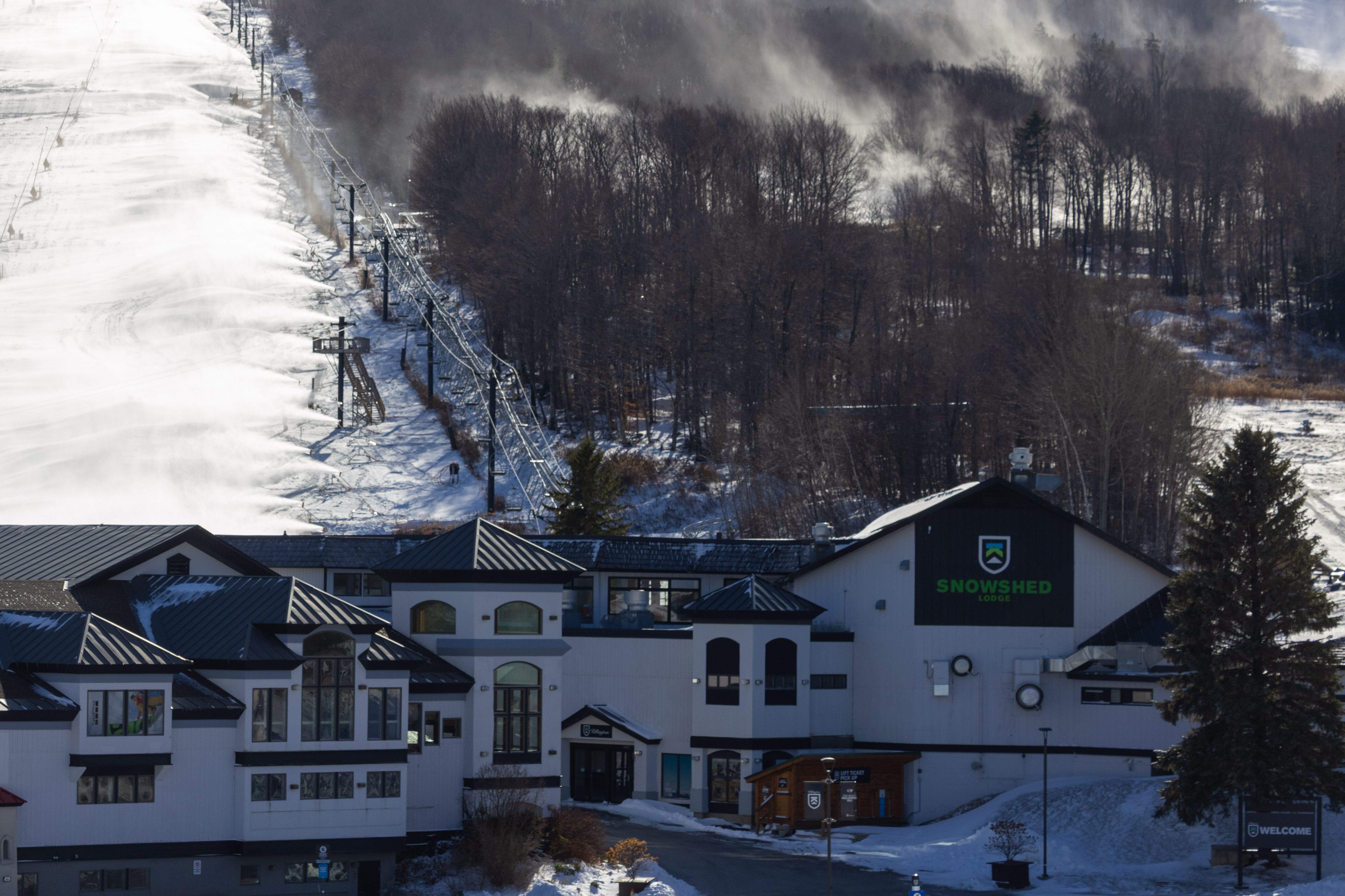 Snowy ski resort with a lodge, ski lift, and snow-making equipment in the background.